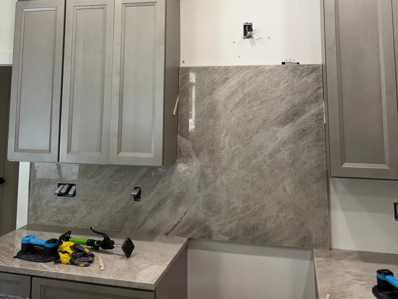 Stone backsplash panel set on the wall between two cabinet stacks, with suction-cup lifters on the counter