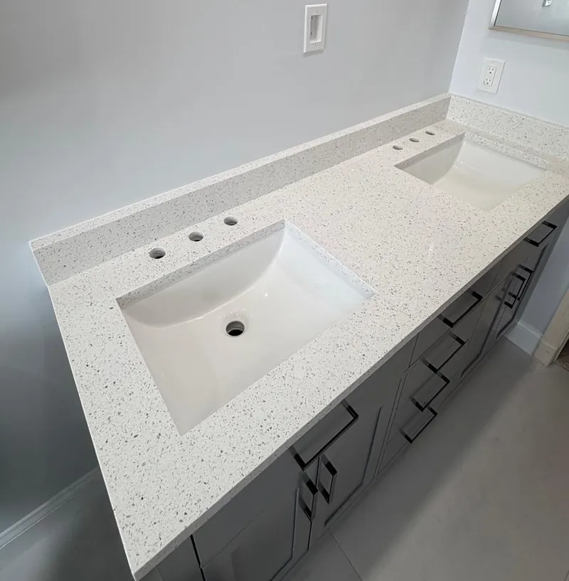 White speckled double vanity top with two undermount sinks, three-hole faucet drilling and a matching backsplash over a gray cabinet