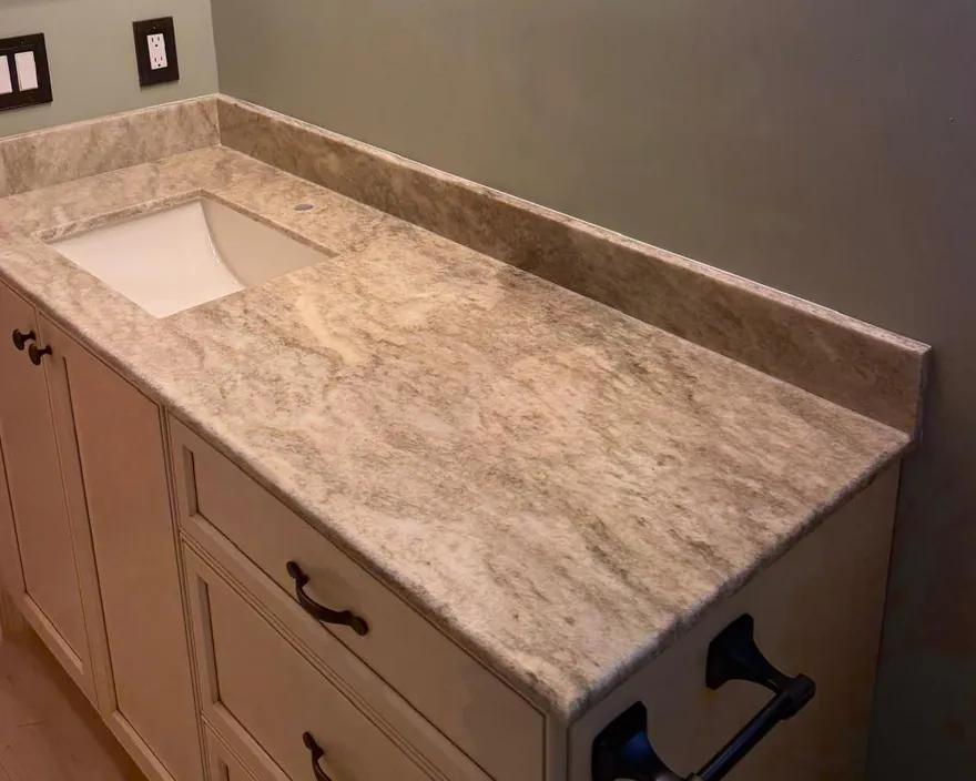Beige and gray veined vanity top with an undermount sink and a matching backsplash on two walls, over cream cabinets with dark pulls