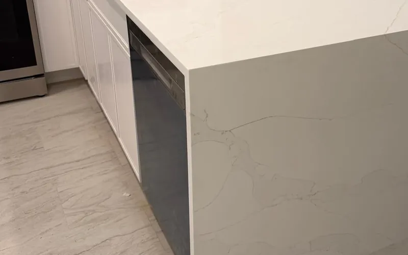 White waterfall peninsula with gray veining next to a black dishwasher