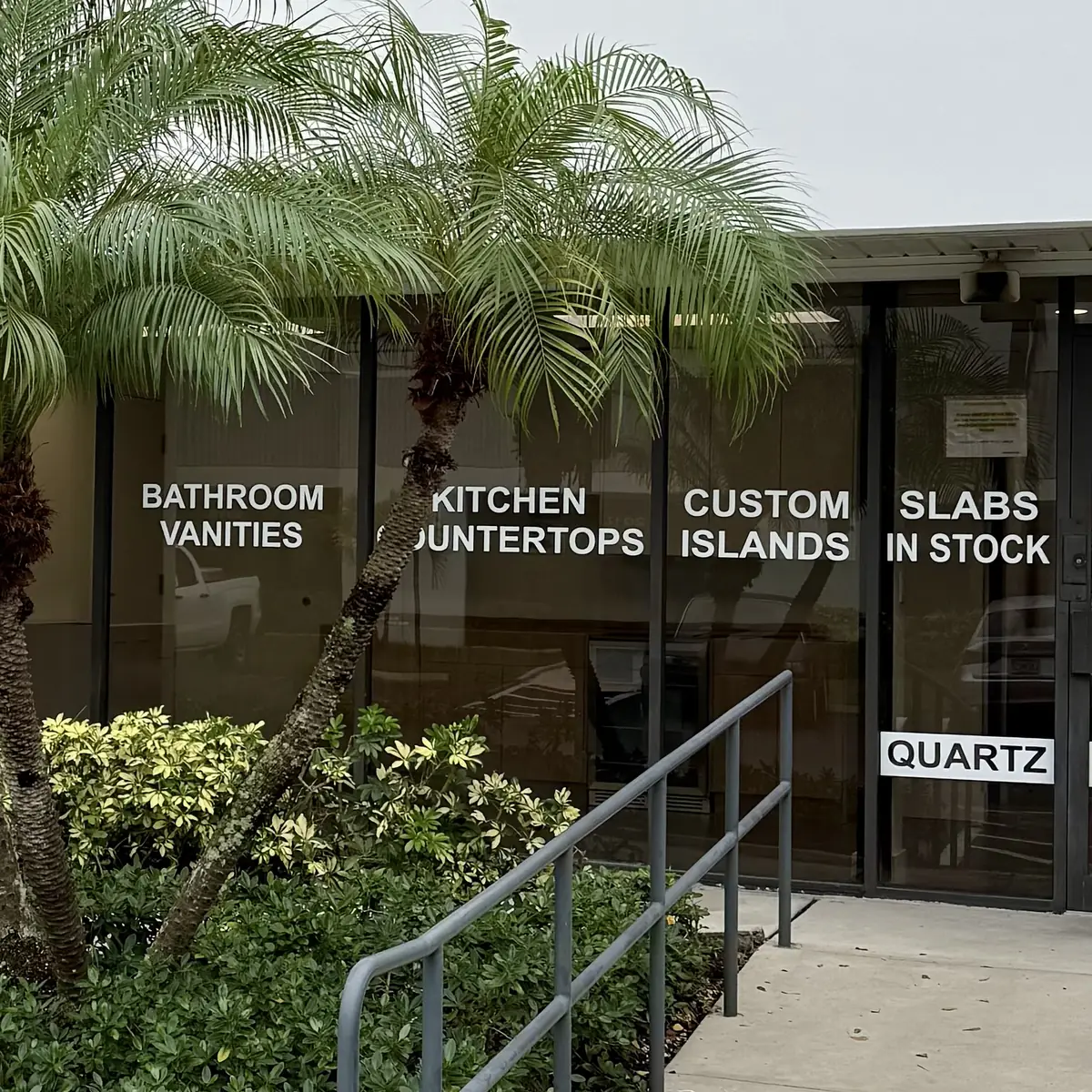 Showroom storefront at 2114 Corporate Dr, Boynton Beach, with windows lettered Bathroom Vanities, Kitchen Countertops, Custom Islands and Slabs in Stock