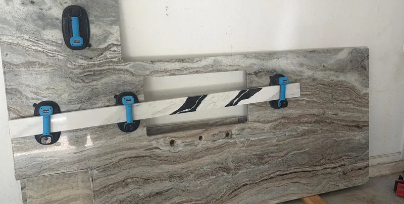 Close-up of a rectangular sink opening and three faucet holes cut into a countertop piece, held upright by suction cups