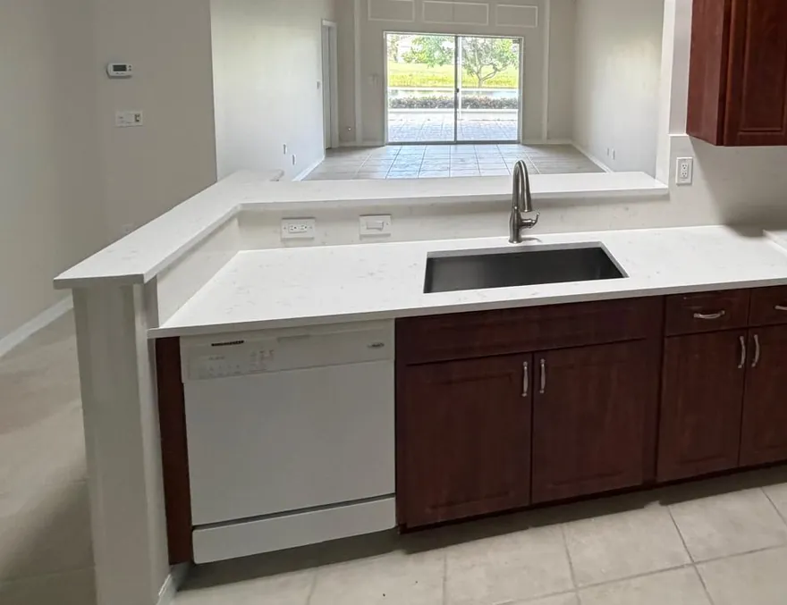 White countertop with an undermount sink and a raised bar ledge on cherry-toned cabinets