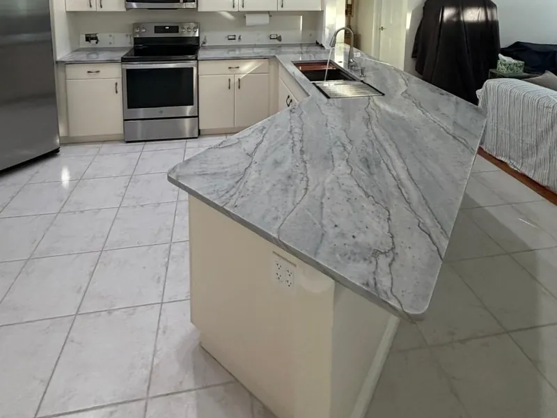 Angled peninsula with long gray veins and an undermount sink, next to a range and a stainless steel refrigerator