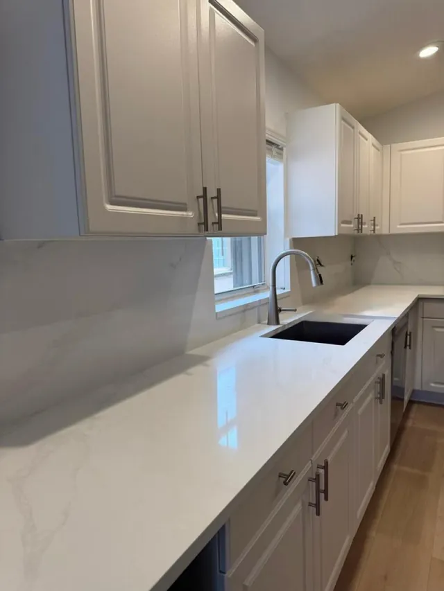 Undermount sink set in a white veined countertop, with a full-height backsplash to match and raised-panel cabinets