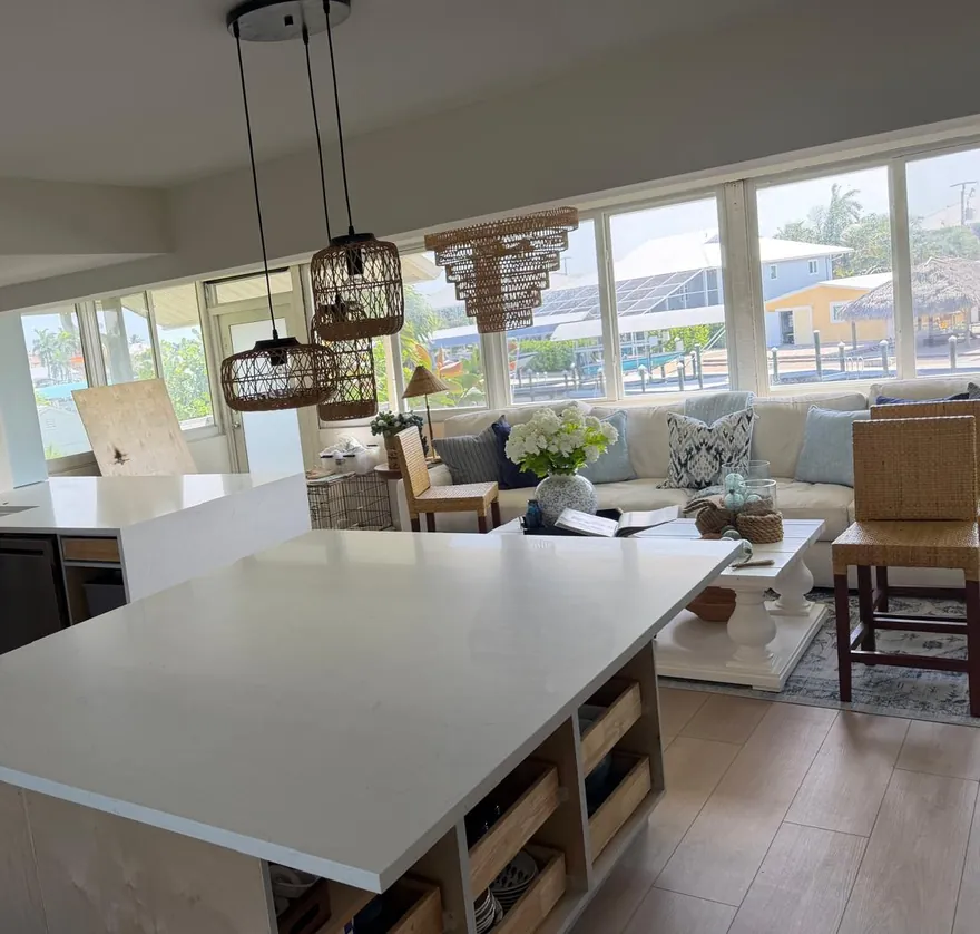 Large white island under woven pendant lights, open to the living room
