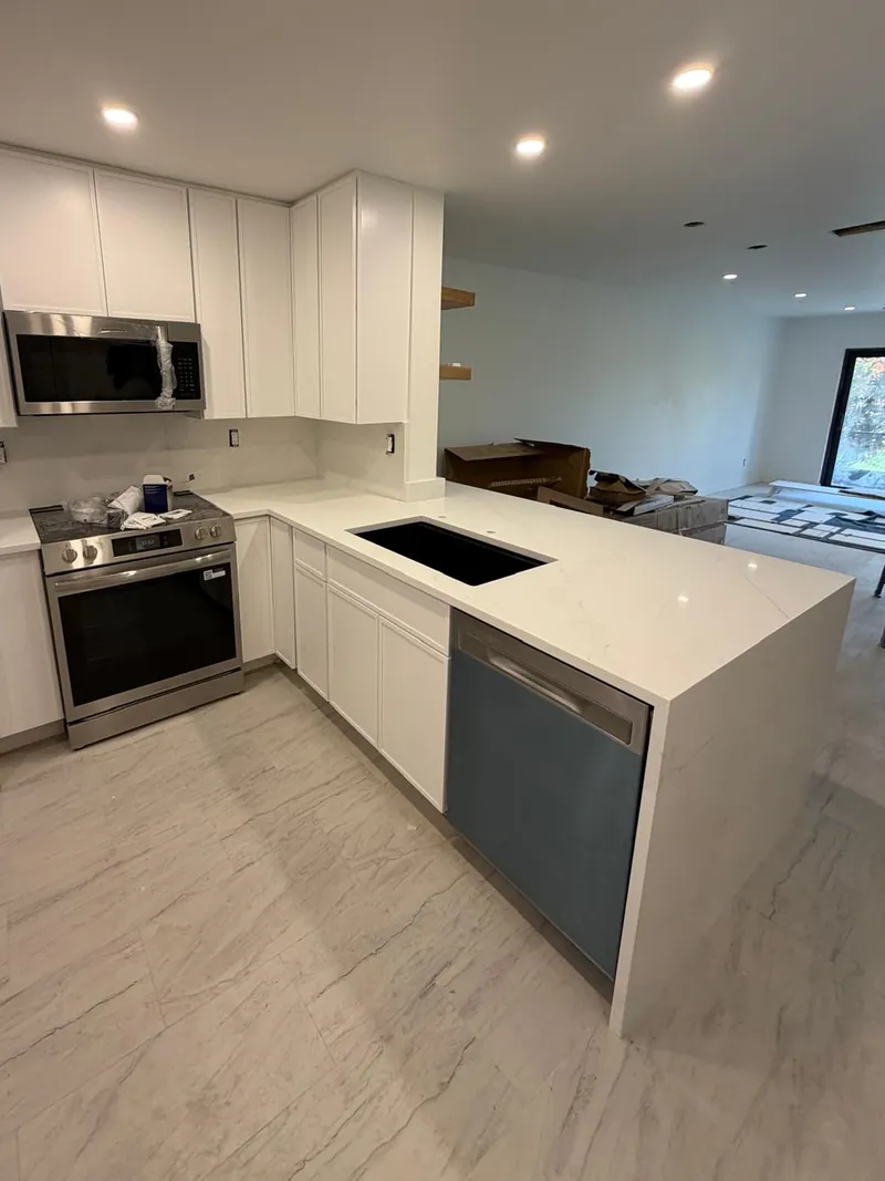 White shaker kitchen with a veined waterfall peninsula, a black sink and a matching full-height backsplash