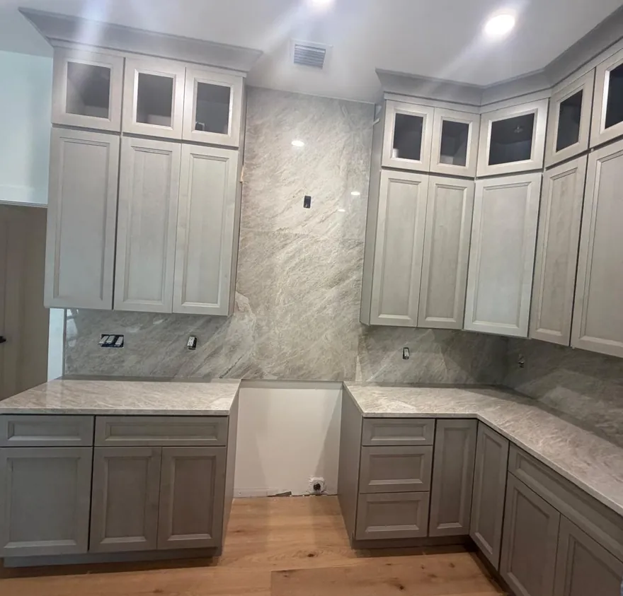 Gray kitchen with light veined countertops and a full-height backsplash between the upper cabinets