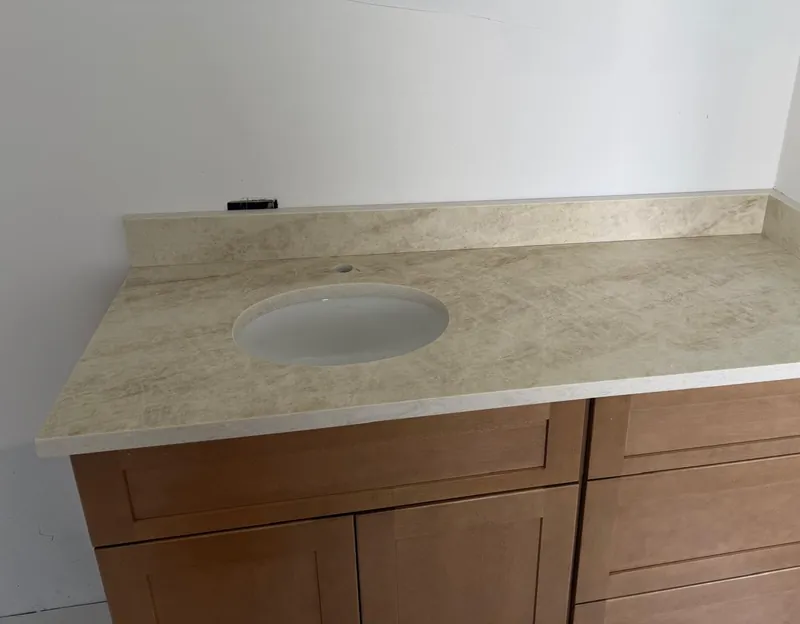Oval undermount sink in a beige veined vanity top, with a side splash, over a shaker-style wood cabinet