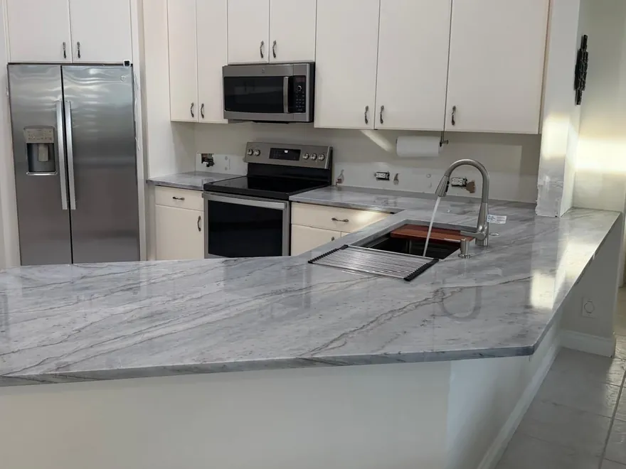 Gray-veined peninsula with an angled end and an undermount sink, in a kitchen with white cabinets