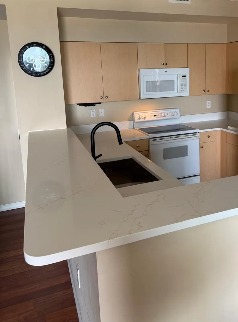 Kitchen peninsula with a white veined countertop, an undermount sink and light wood cabinets