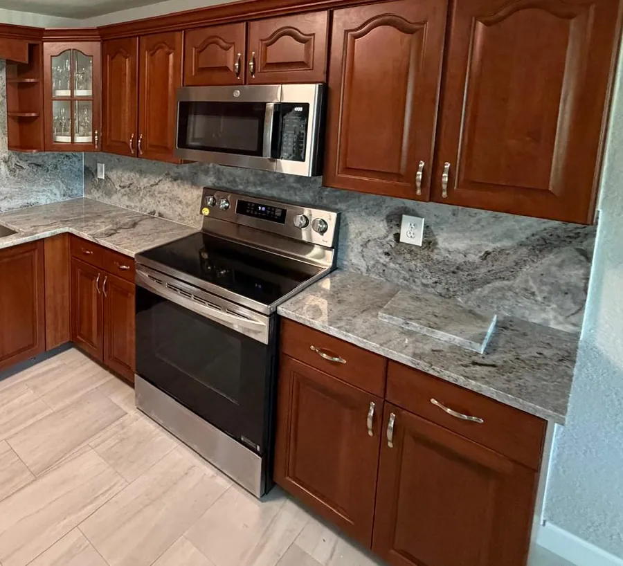 Kitchen with gray and white stone countertops, a full-height stone backsplash and cherry cabinets