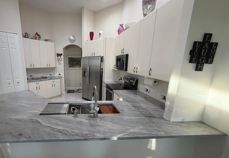 Gray veined stone peninsula with an undermount workstation sink and white cabinets