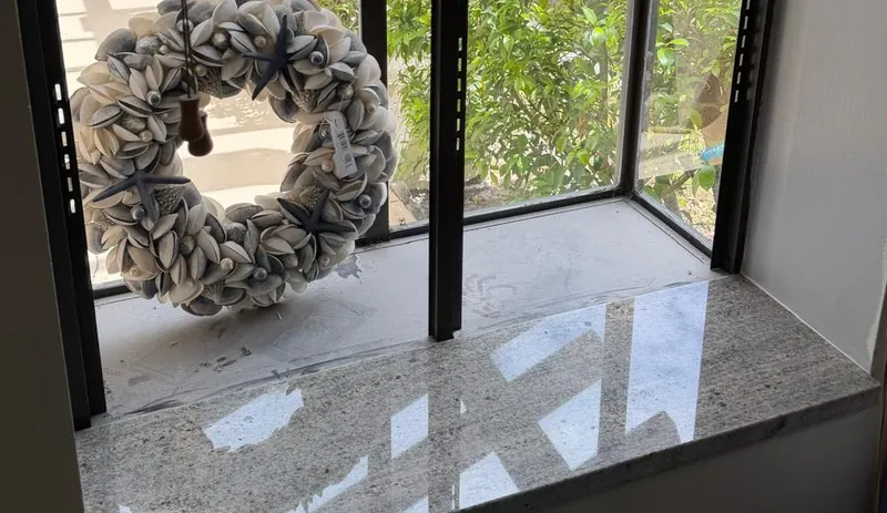 Polished stone window sill seen from above, with a shell wreath in the window