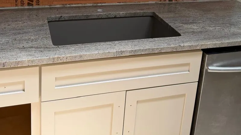 Speckled gray stone countertop with a black undermount sink and cream shaker cabinets, before the backsplash goes on