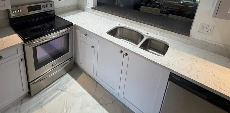 White shaker kitchen with a light veined countertop, a double-bowl undermount sink and a pass-through to the living room