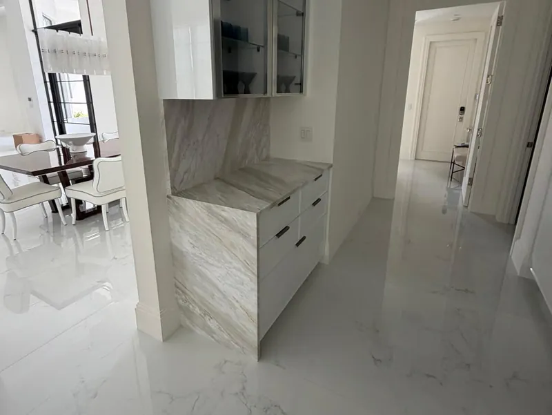 Built-in hallway cabinet with a veined top, a waterfall side and a matching backsplash under glass-front uppers