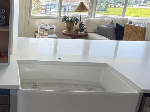 White countertop cut around an apron-front farmhouse sink, open to a living room beyond