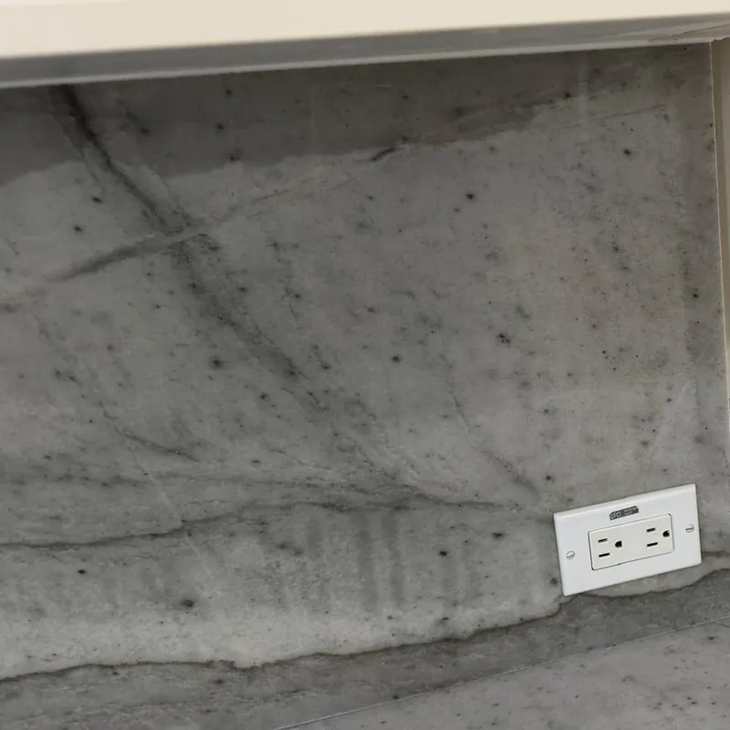 Close-up of a gray veined backsplash with an outlet opening cut into the stone