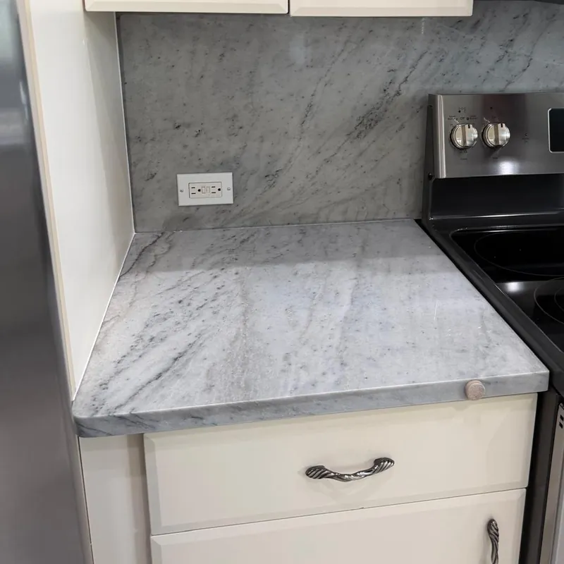 Finished corner with a gray veined countertop and matching backsplash beside a stainless range