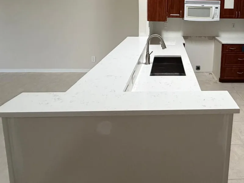 L-shaped white countertop with an undermount sink in the peninsula and cherry-toned cabinets