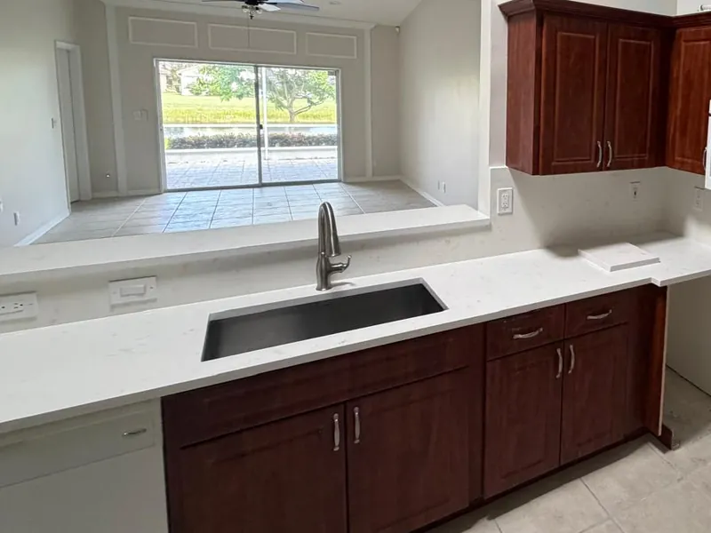 White countertop with an undermount sink below a pass-through, next to cherry-toned cabinets
