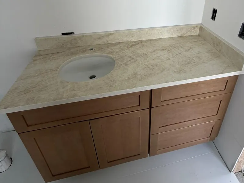Beige veined vanity top with an oval undermount sink and a matching low backsplash on a wood cabinet