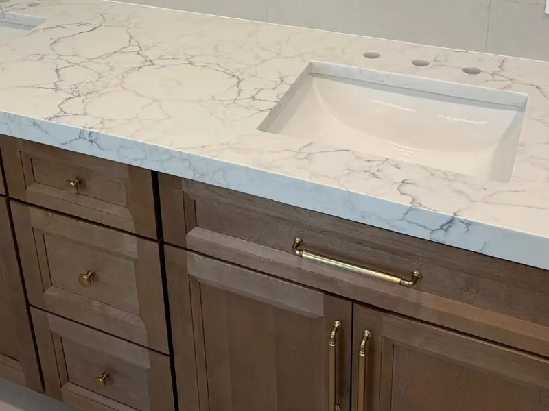 White countertop with fine gray veining and an undermount sink on a wood double vanity with brass pulls