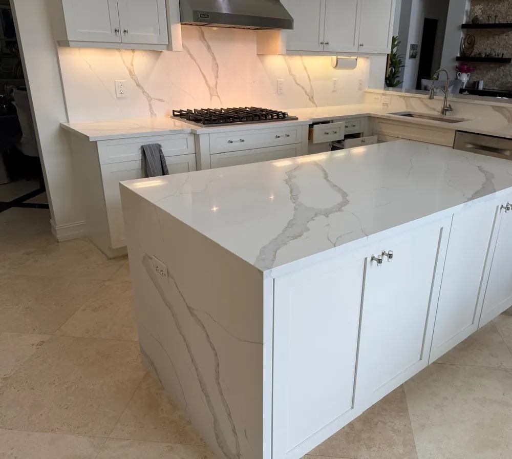 Waterfall island with soft gray veining, a matching full-height backsplash and white shaker cabinets