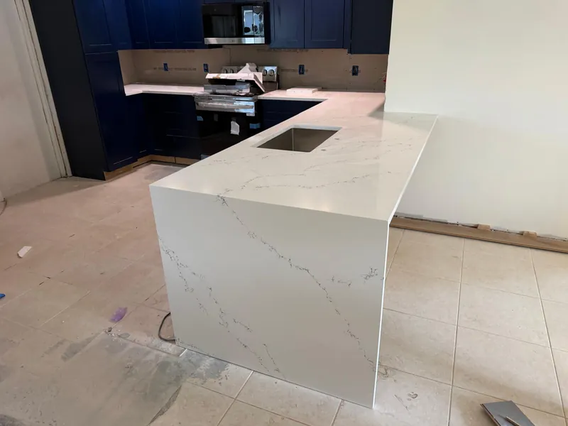 White veined waterfall peninsula with an undermount sink and navy cabinets