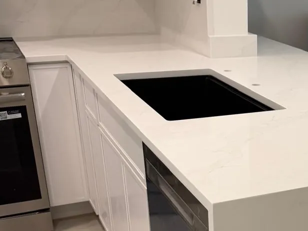White countertop with soft gray veining, a black undermount sink and a matching backsplash