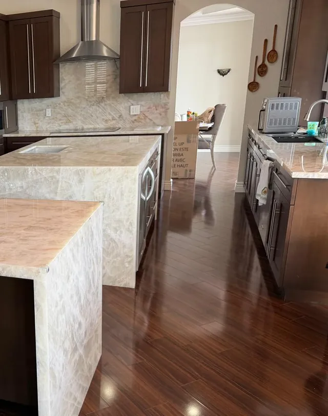 A light veined island and peninsula with waterfall sides, a full-height veined backsplash and dark wood cabinets