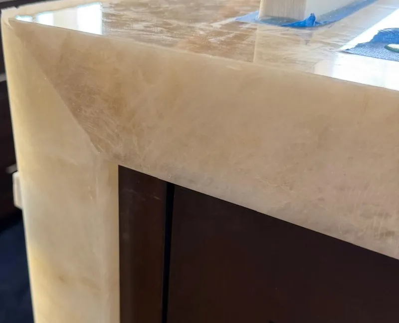 Mitered corner joining a light veined countertop to its waterfall side, above a dark wood cabinet