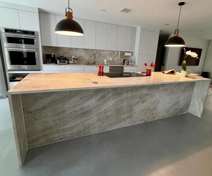 Taj Mahal quartzite island with waterfall sides at both ends, white flat-panel cabinets and black pendant lights