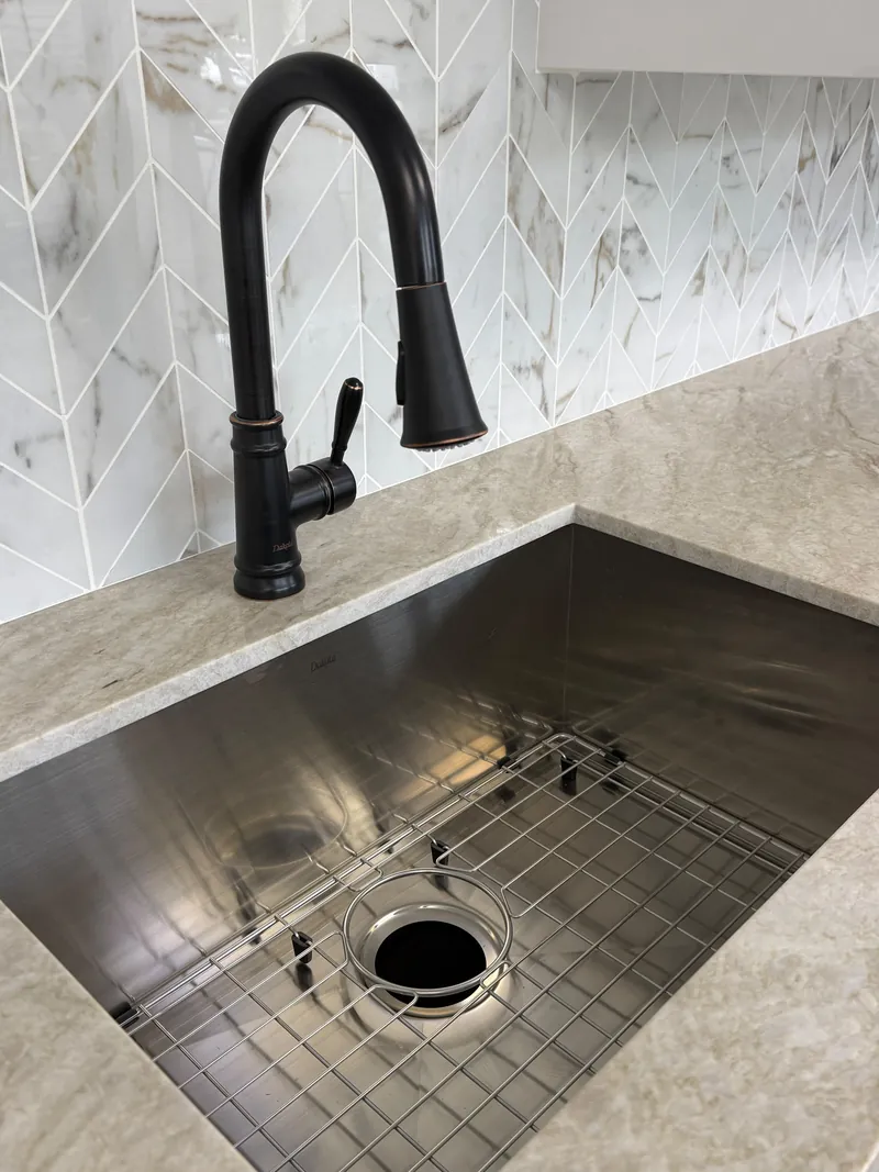 Stainless steel undermount sink with a bottom grid set into a veined countertop, under a dark bronze pull-down faucet