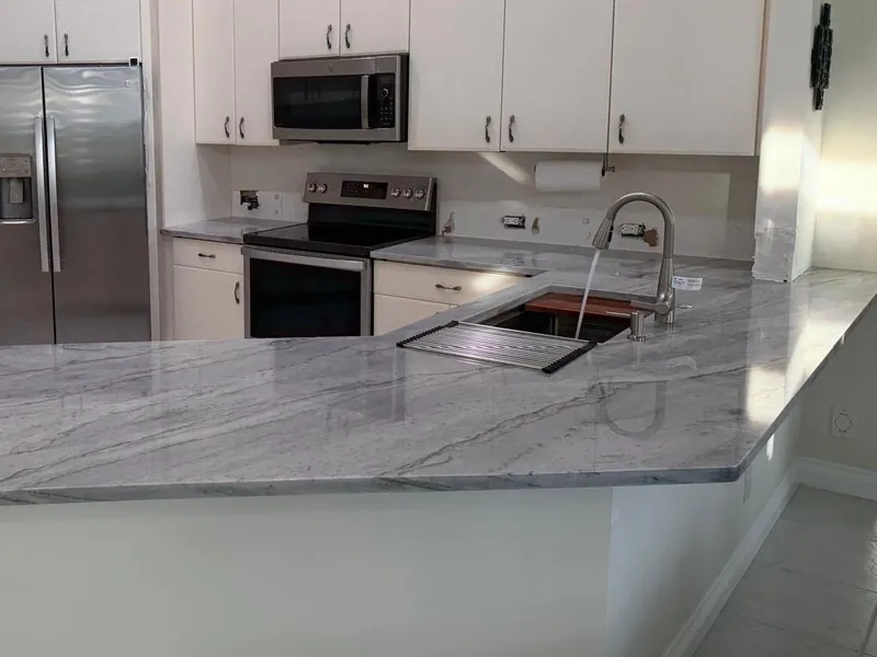 Gray veined peninsula with a sink fitted with a cutting board and a drying rack, under white cabinets