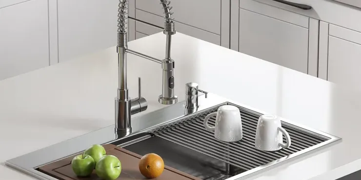 Stainless steel drop-in sink with its rim on a white counter, fitted with a cutting board and a drying rack, manufacturer photo